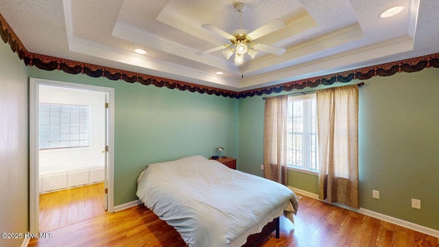 bedroom featuring a tray ceiling, light wood-style flooring, crown molding, and baseboards