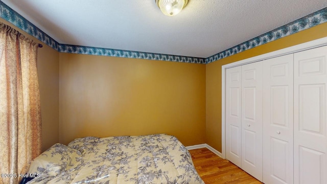 bedroom featuring a closet, baseboards, a textured ceiling, and wood finished floors