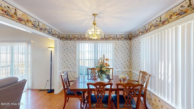 dining room featuring light wood finished floors, a textured ceiling, baseboards, and ornamental molding