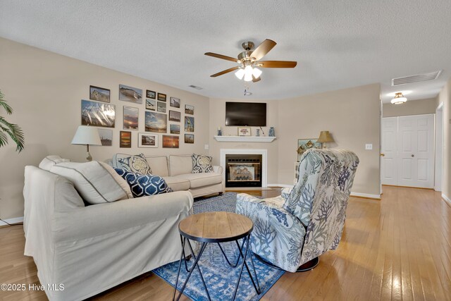 222 NE 36th St, Oak Island, NC 28465 - living area with a textured ceiling, ceiling fan, visible vents, a glass covered fireplace, and light wood-type flooring
