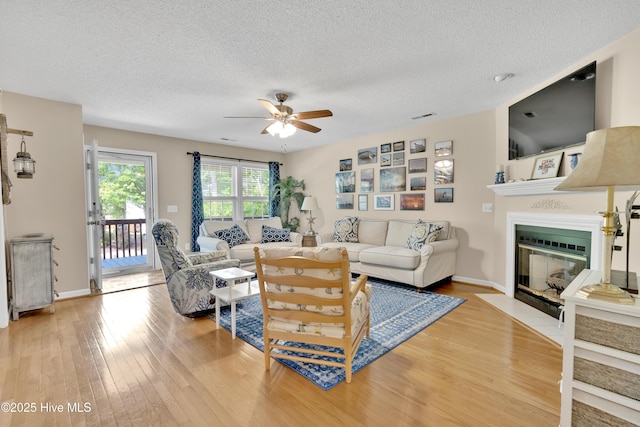 222 NE 36th St, Oak Island, NC 28465 - living room featuring a fireplace with flush hearth, a textured ceiling, ceiling fan, baseboards, and light wood-type flooring