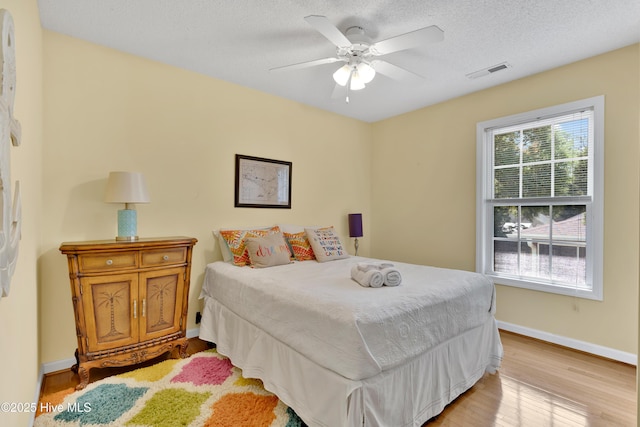 222 NE 36th St, Oak Island, NC 28465 - bedroom with ceiling fan, light wood-type flooring, visible vents, baseboards, and a textured ceiling