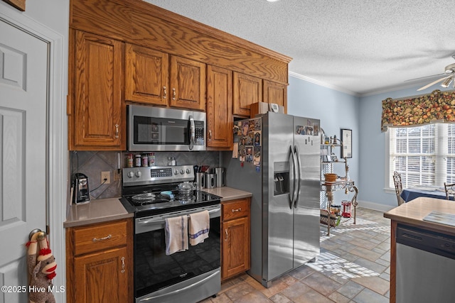 kitchen with a ceiling fan, brown cabinets, appliances with stainless steel finishes, stone finish flooring, and tasteful backsplash