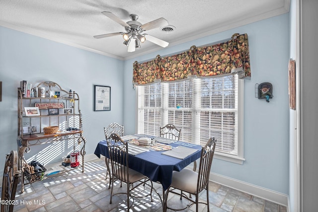 dining area with a textured ceiling, stone tile floors, crown molding, baseboards, and ceiling fan