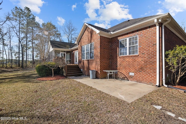 rear view of property featuring a patio, a lawn, and brick siding