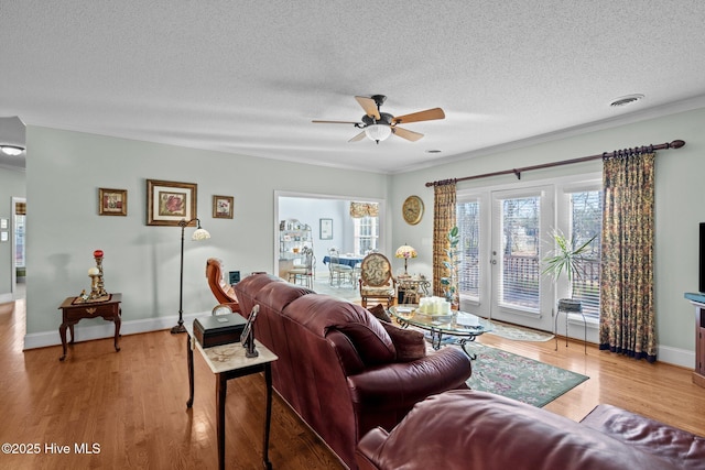 living area featuring light wood finished floors, visible vents, baseboards, ceiling fan, and a textured ceiling