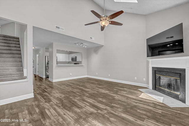 6211 Wrightsville Ave Unit 111, Wilmington, NC 28403 - unfurnished living room featuring a fireplace with flush hearth, wood finished floors, stairway, ceiling fan, and high vaulted ceiling
