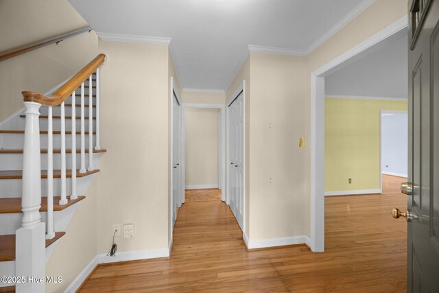 corridor featuring light wood-style floors, baseboards, crown molding, and stairs
