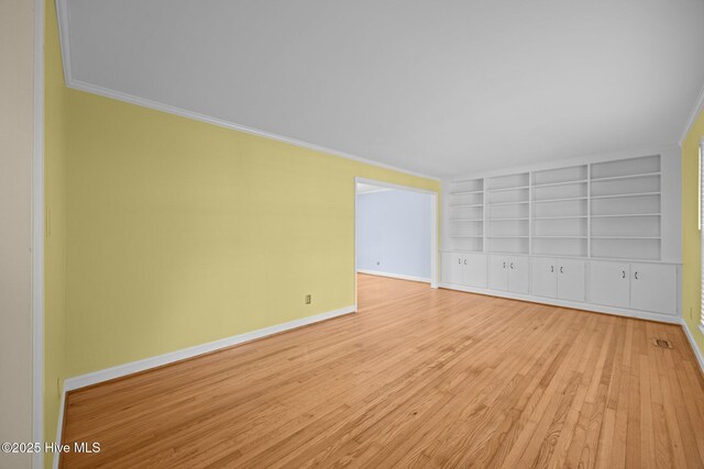 unfurnished room with baseboards, built in shelves, ornamental molding, and light wood-style floors