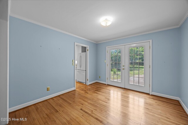 empty room with crown molding, french doors, light wood-style flooring, baseboards, and visible vents