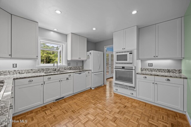 kitchen featuring visible vents, a sink, white cabinetry, and white appliances