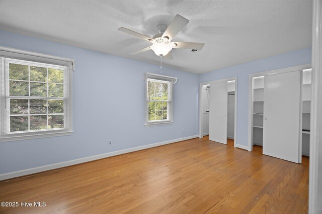 unfurnished bedroom featuring baseboards, light wood-style flooring, multiple closets, and multiple windows