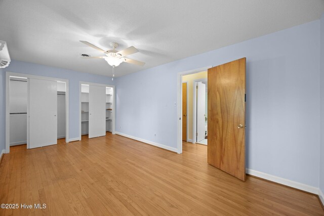 unfurnished bedroom featuring light wood-style floors, baseboards, ceiling fan, and two closets