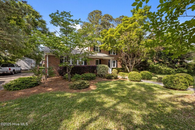 view of property hidden behind natural elements with brick siding and a front lawn