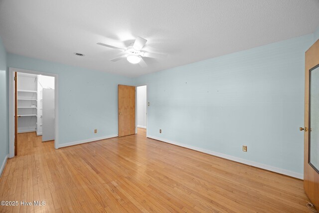 unfurnished bedroom featuring a ceiling fan, baseboards, a closet, a spacious closet, and light wood-style flooring