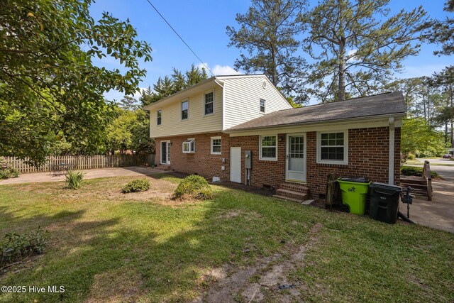 back of house featuring a lawn, brick siding, fence, and entry steps