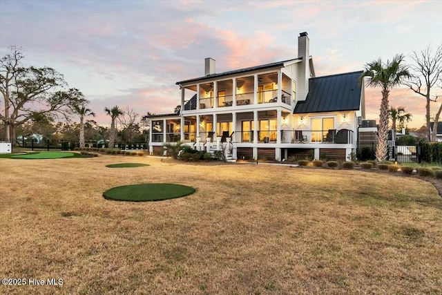 7522 Dunbar Rd, Wilmington, NC 28411 - back of house at dusk featuring a balcony, a chimney, and a lawn