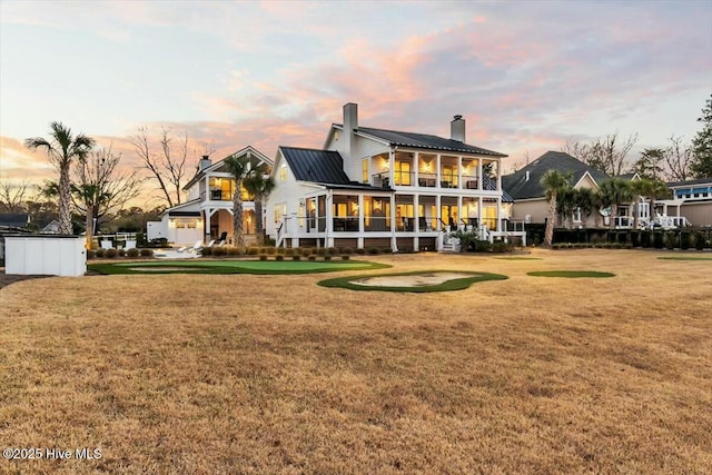 7522 Dunbar Rd, Wilmington, NC 28411 - back of property at dusk with a chimney, a sunroom, and a lawn