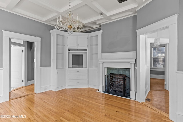 unfurnished living room featuring beam ceiling, light wood-type flooring, a tiled fireplace, coffered ceiling, and a notable chandelier