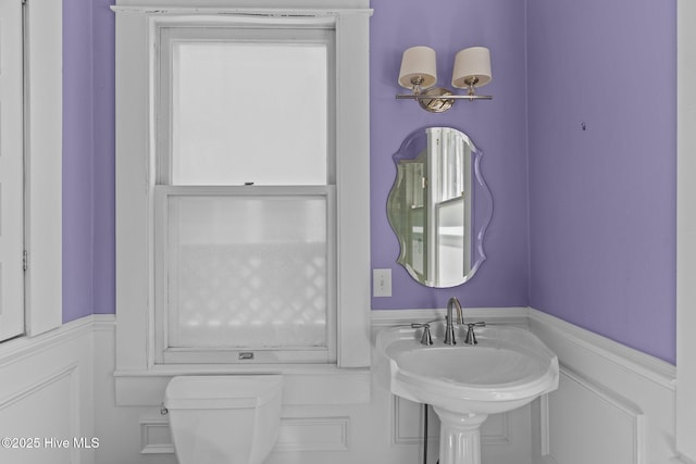 half bathroom featuring toilet, a sink, and a wainscoted wall
