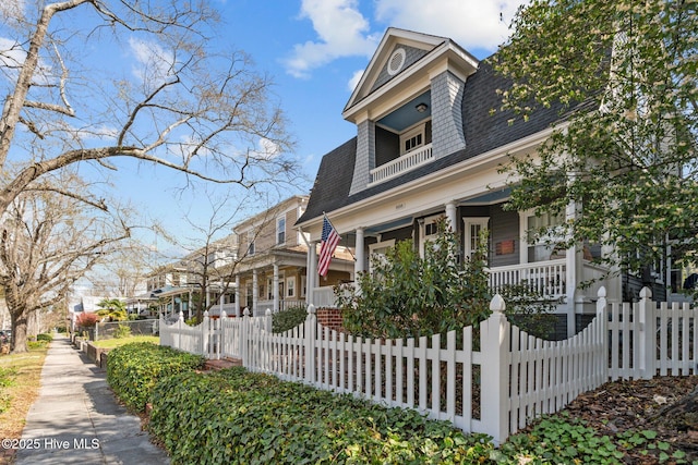 view of front facade with a porch, a fenced front yard, a balcony, and roof with shingles