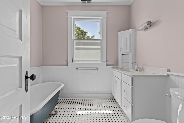full bathroom featuring vanity, ornamental molding, toilet, a freestanding bath, and a wainscoted wall