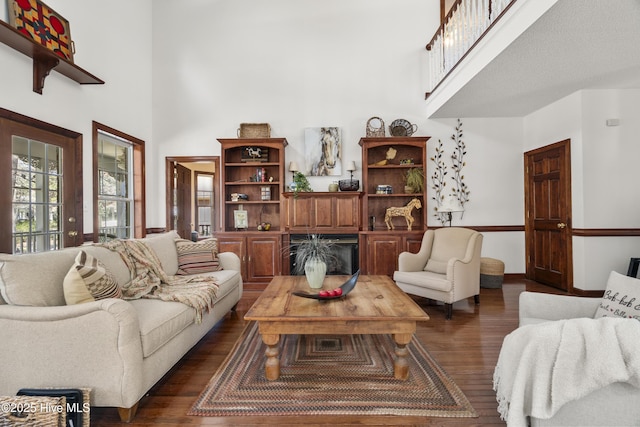 living area featuring baseboards, a fireplace, a towering ceiling, and dark wood finished floors
