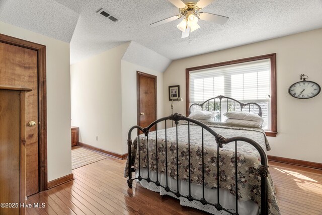 bedroom with a textured ceiling, visible vents, hardwood / wood-style flooring, baseboards, and a ceiling fan
