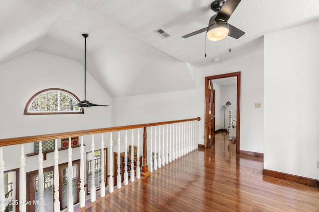 hall featuring vaulted ceiling, a textured ceiling, baseboards, visible vents, and hardwood / wood-style floors