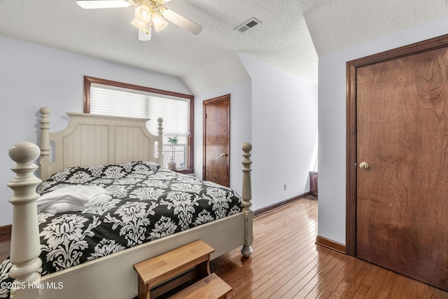 bedroom with lofted ceiling, wood-type flooring, baseboards, a textured ceiling, and visible vents