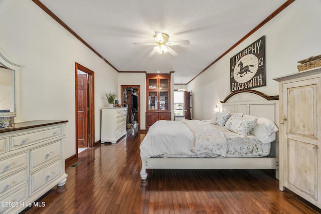 bedroom with a walk in closet, ornamental molding, baseboards, dark wood finished floors, and a ceiling fan
