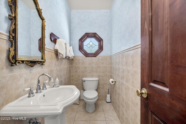 half bathroom with tile walls, toilet, tile patterned flooring, and a sink