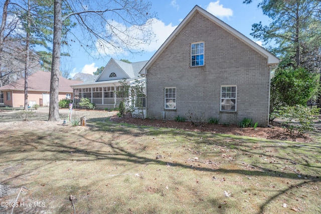 rear view of property featuring a lawn, a sunroom, and brick siding