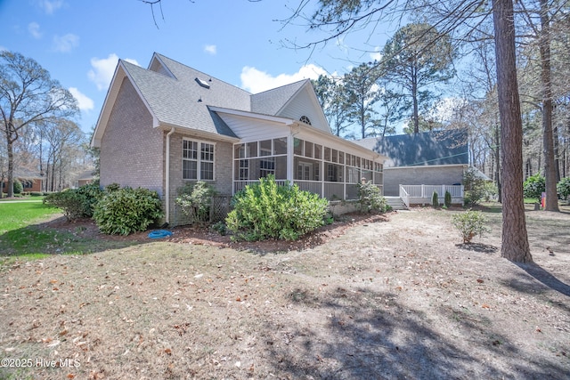 back of house with a sunroom, brick siding, and roof with shingles