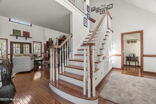 stairs with hardwood / wood-style floors, high vaulted ceiling, and baseboards