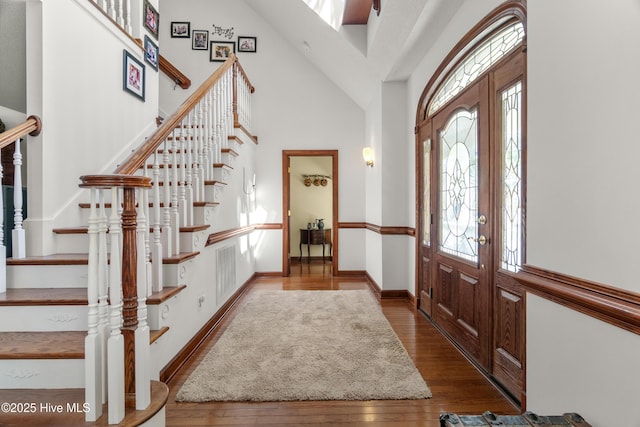 entryway featuring high vaulted ceiling, visible vents, hardwood / wood-style flooring, baseboards, and stairs