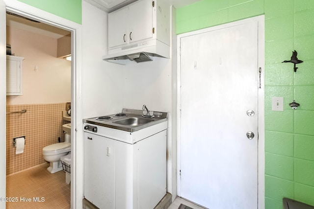 clothes washing area with a sink, tile walls, light tile patterned flooring, and a wainscoted wall