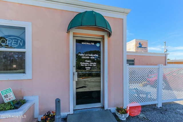 entrance to property featuring stucco siding and fence