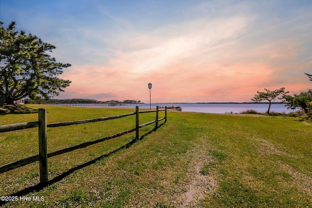 yard at dusk featuring a water view and fence