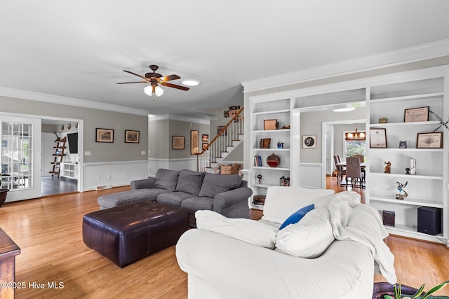 living room with stairs, light wood-style flooring, ceiling fan with notable chandelier, and crown molding