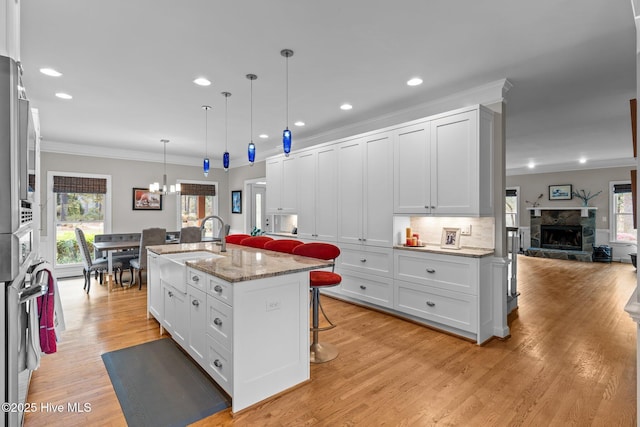 kitchen with a breakfast bar, a chandelier, plenty of natural light, crown molding, and light wood-style floors