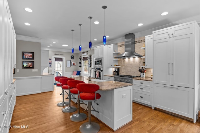 kitchen featuring wall chimney range hood, light wood finished floors, ornamental molding, and appliances with stainless steel finishes