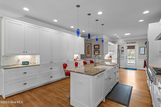 kitchen featuring white cabinets, a sink, ornamental molding, light wood-type flooring, and a center island with sink