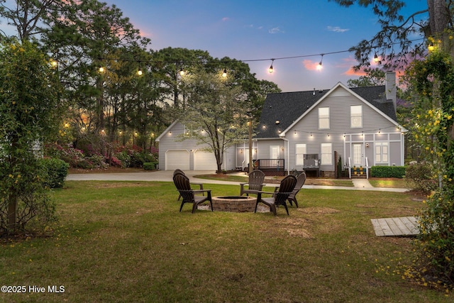 back of house with an outbuilding, a garage, a yard, a fire pit, and concrete driveway