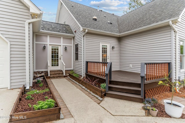 view of exterior entry with roof with shingles, a garage, and a deck
