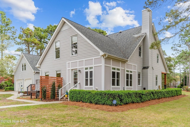 exterior space with a chimney, a garage, a lawn, and roof with shingles