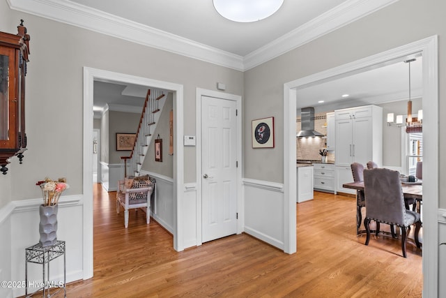 interior space with ornamental molding, a chandelier, a wainscoted wall, stairs, and light wood finished floors