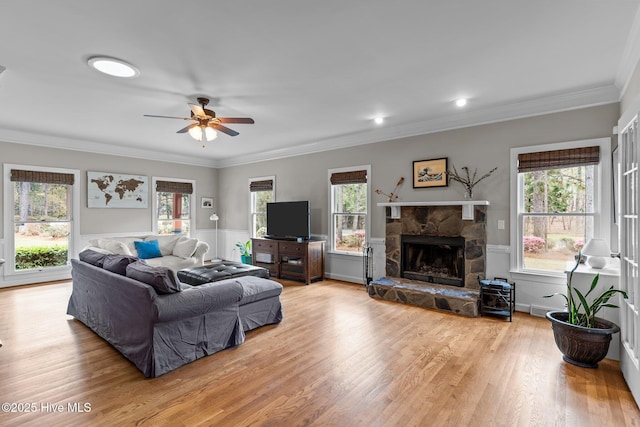 living room with a healthy amount of sunlight, light wood finished floors, a stone fireplace, and ceiling fan
