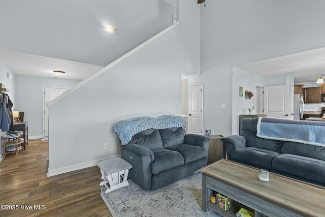 living area with baseboards, a towering ceiling, and dark wood finished floors