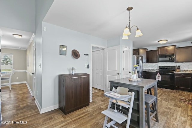 kitchen with a notable chandelier, dark brown cabinetry, wood finished floors, baseboards, and black appliances